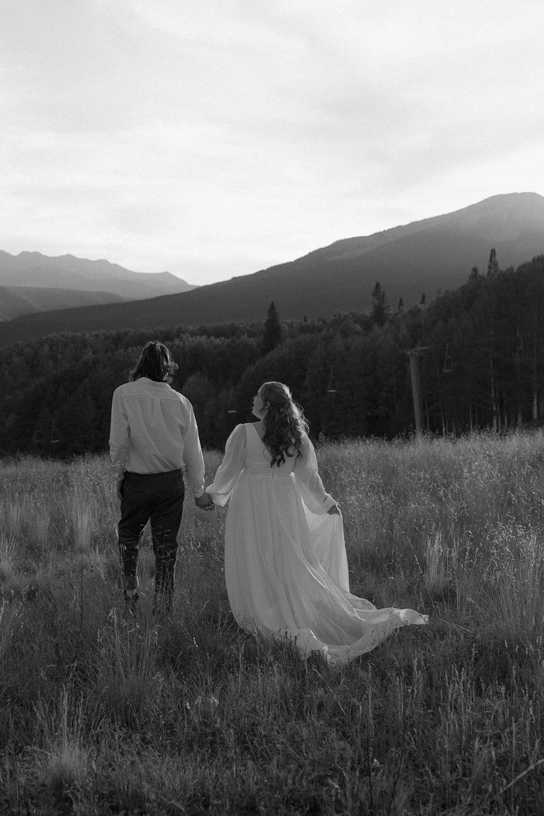 Black and white photo of a couple walking hand in hand through a mountain meadow in Crested Butte, highlighting documentary elopement photography and intimate Colorado wedding moments.