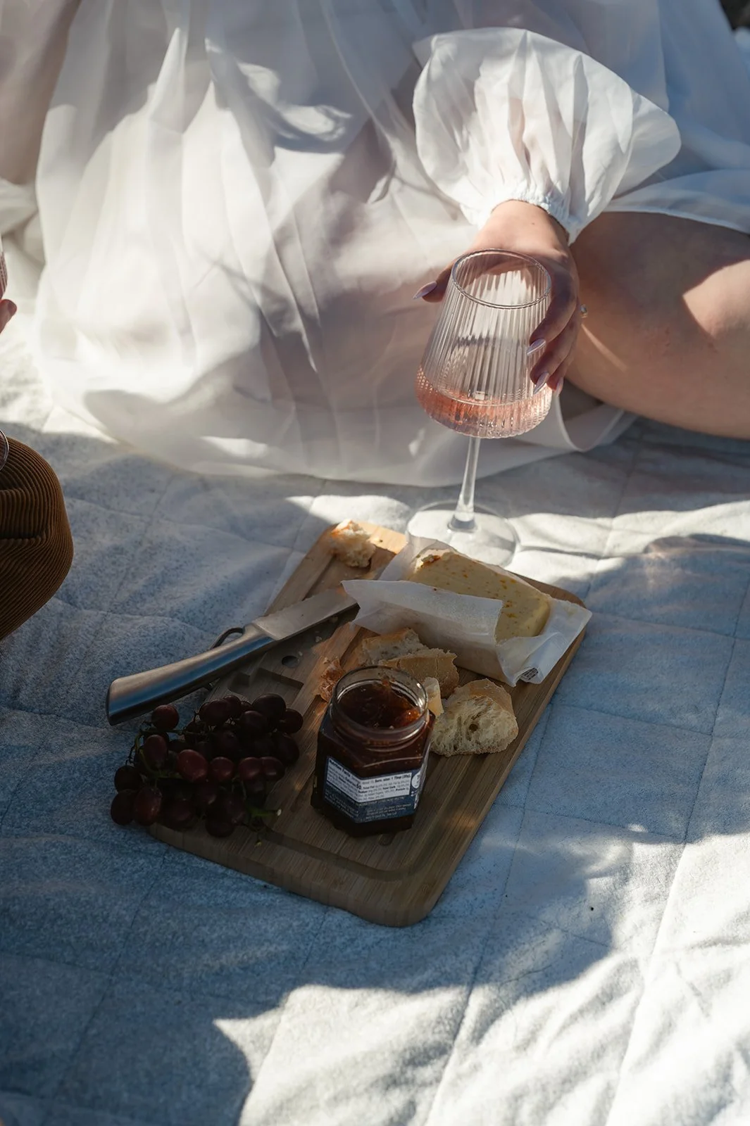Detail photo of a bride sitting on a picnic blanket holding a wine glass, with a charcuterie board and grapes during a romantic Crested Butte elopement picnic.