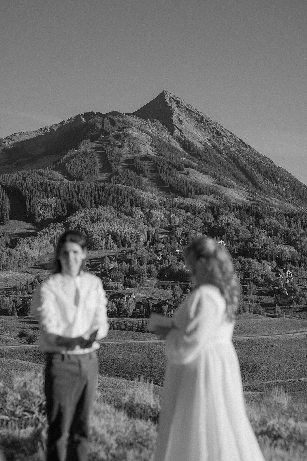 Couple standing in front of Mount Crested Butte during their Crested Butte elopement, with the mountain towering in the background and the town below in soft focus.