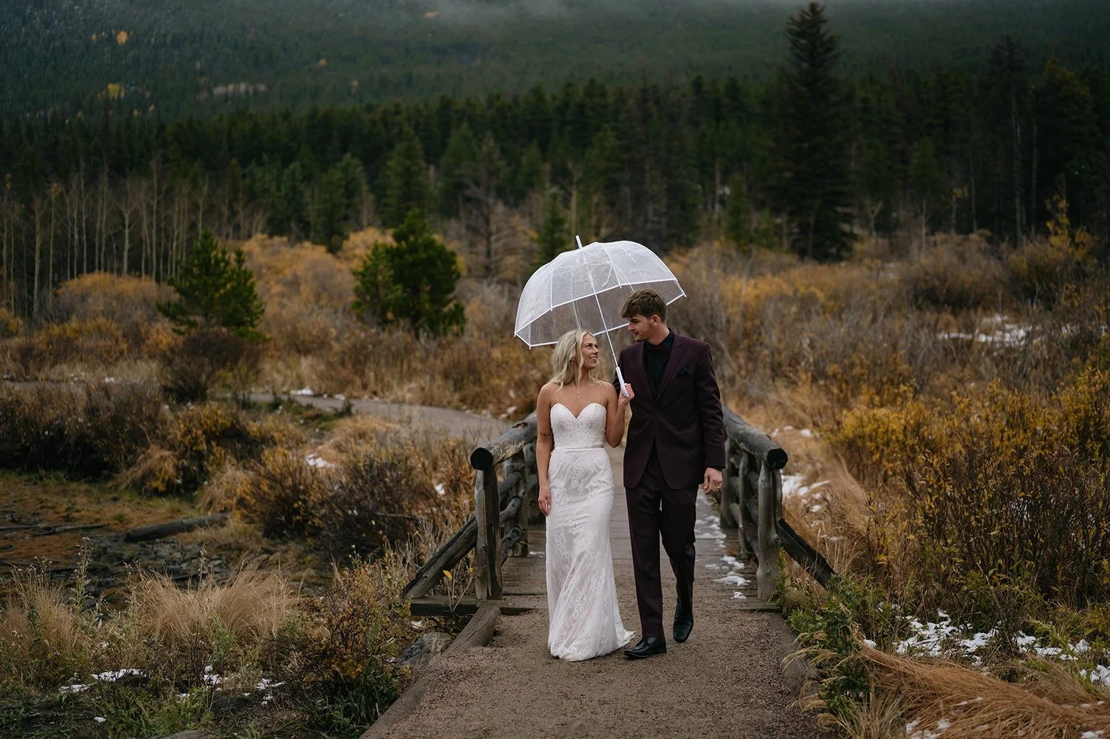 newlyweds walking underneath an umbrella in the Colorado mountains