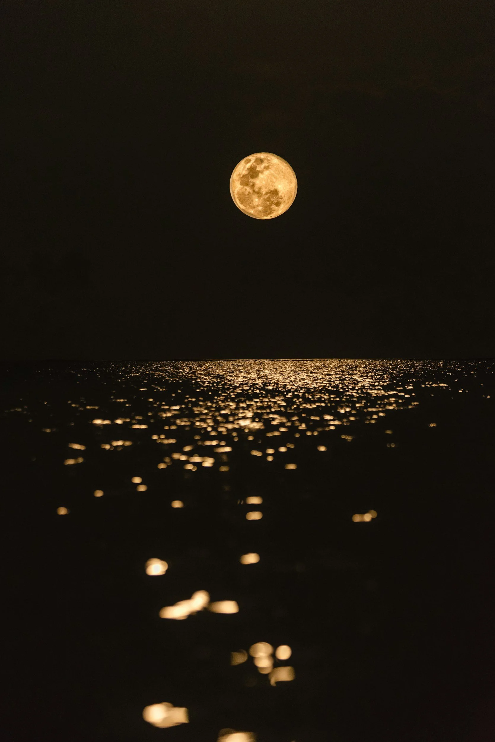 Full moon over the ocean, with the reflection of moonlight shimmering on the water's surface.