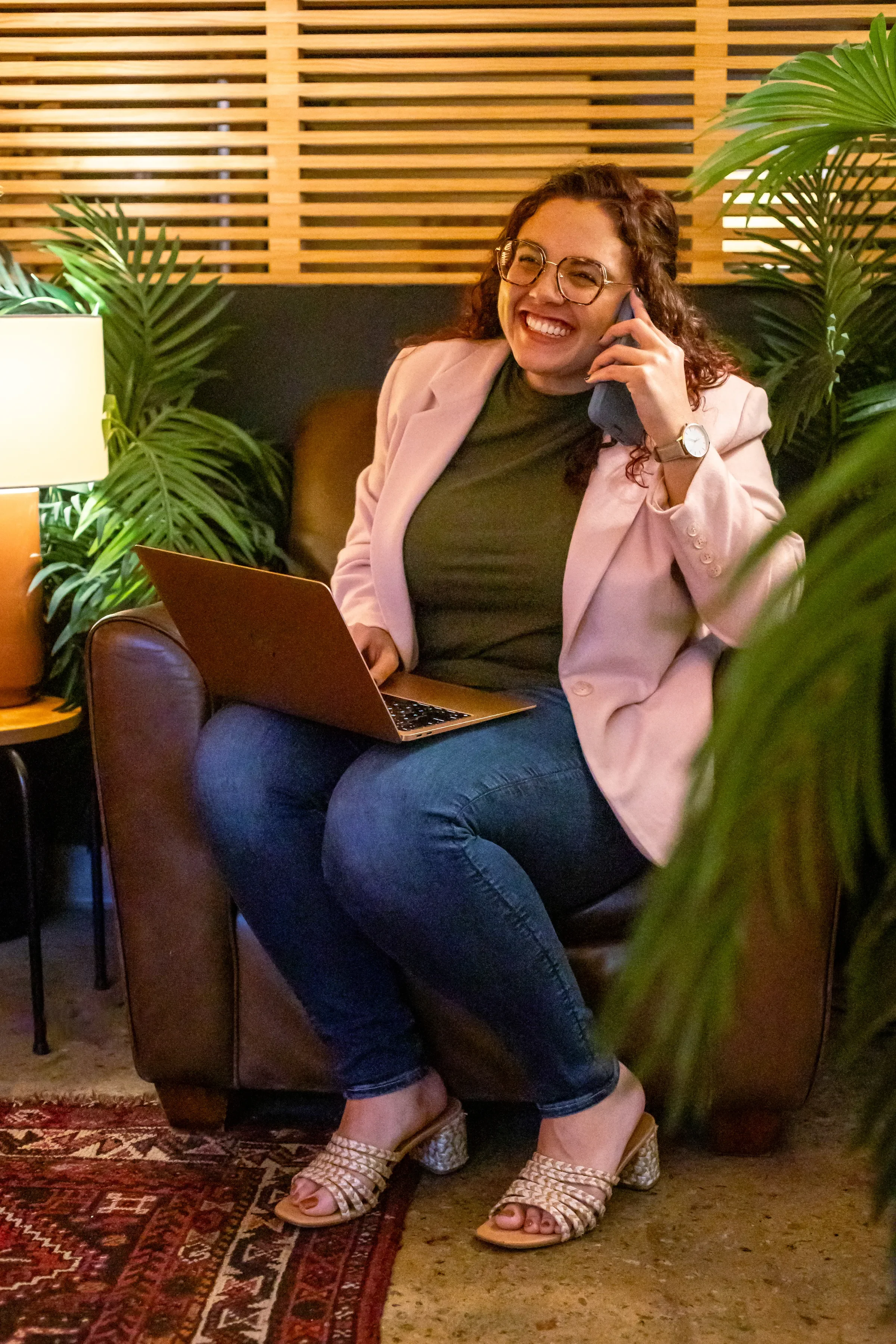 Raven sits in an Atlanta coworking space on her laptop and on the phone smiling while doing work.