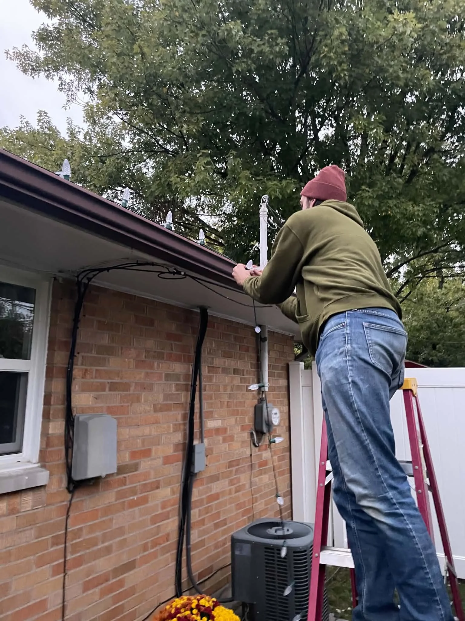 1. Professional Christmas light installer placing C9 holiday lights along the roofline of a brick home in Dayton, Ohio.