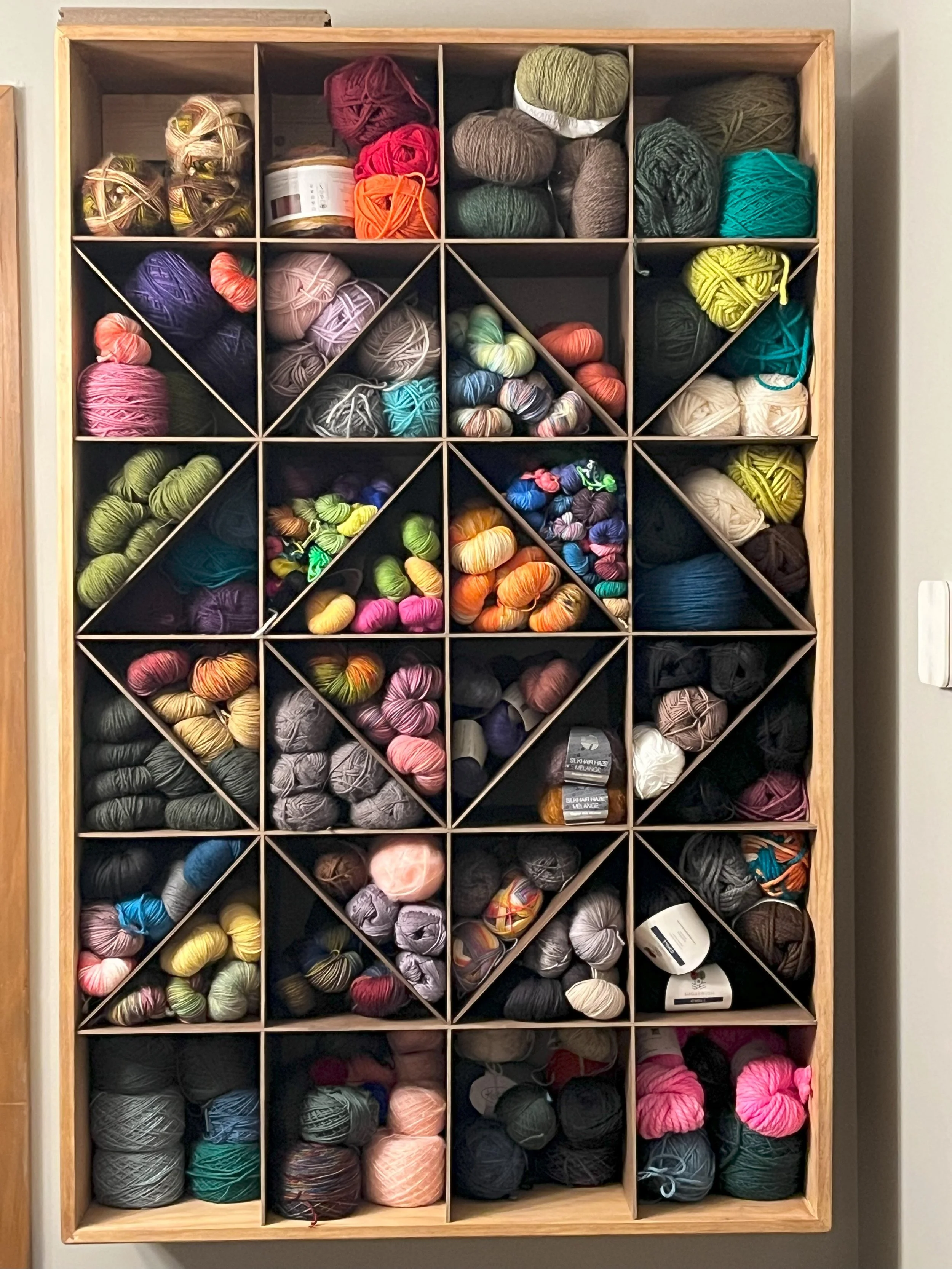 Multiple colors of yarn in a wall mounted wooden yarn storage unit