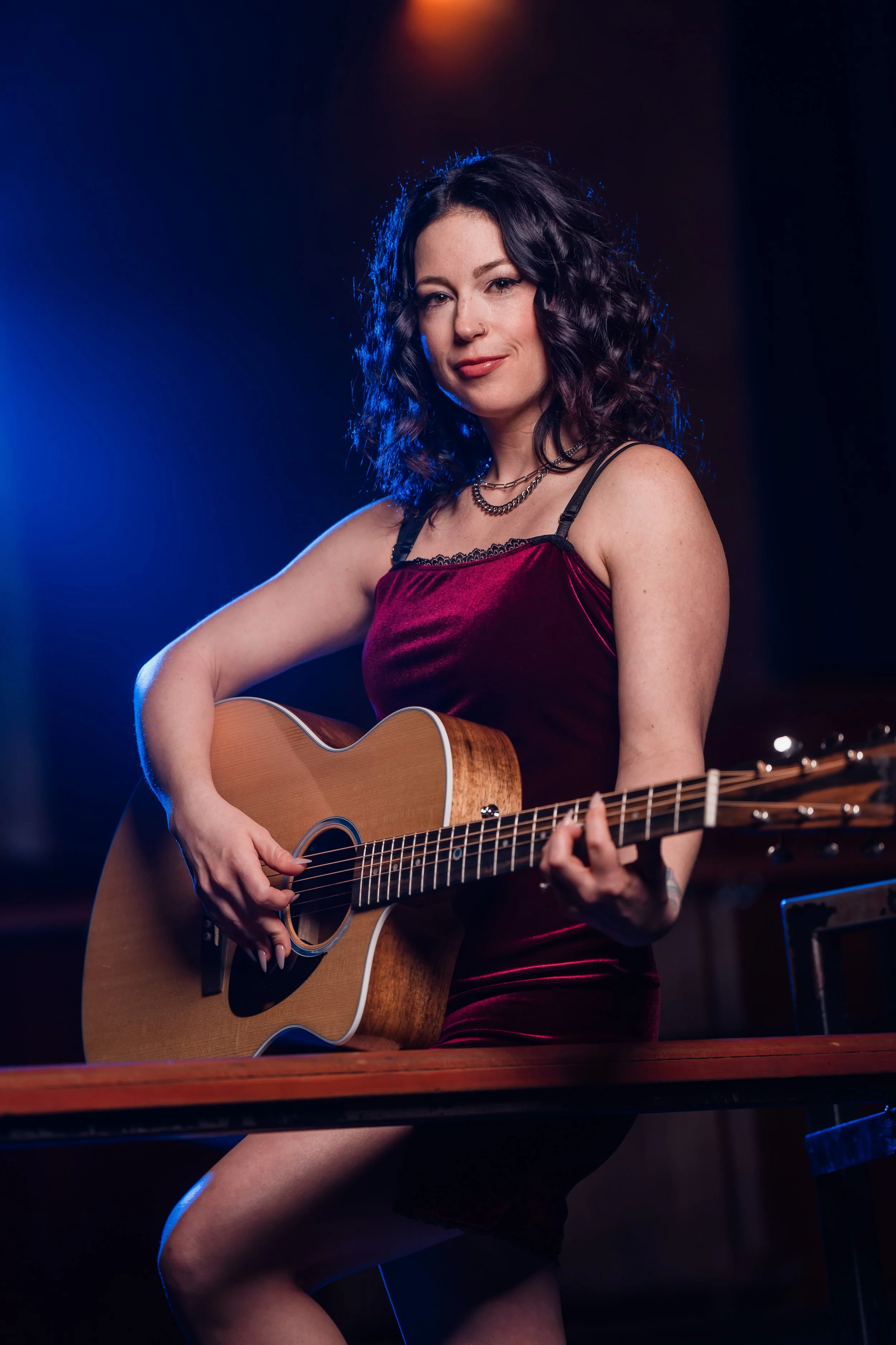 Woman in a red dress playing acoustic guitar in a dimly lit room.