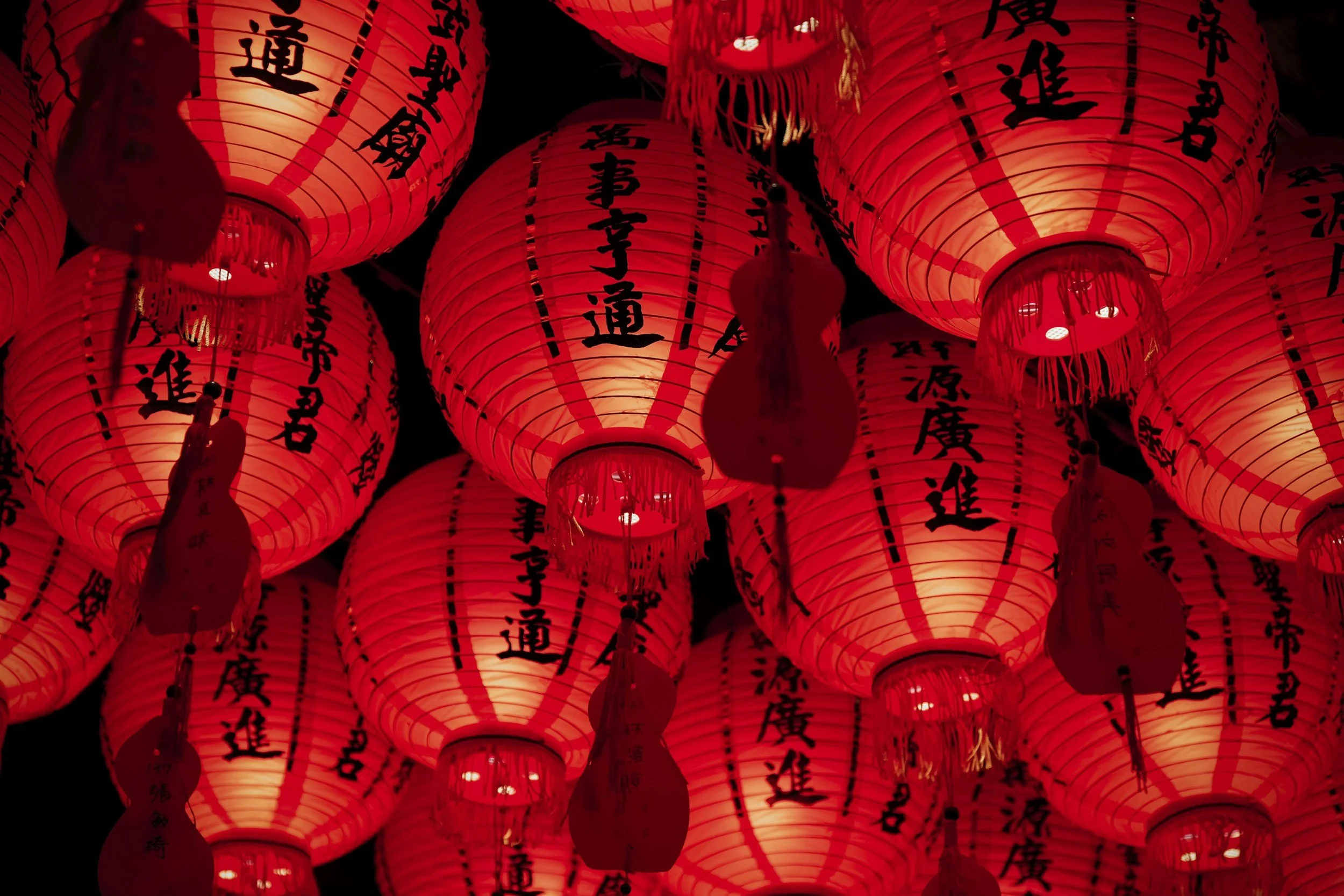 Multiple red paper lanterns with black Chinese characters hanging in the darkness.