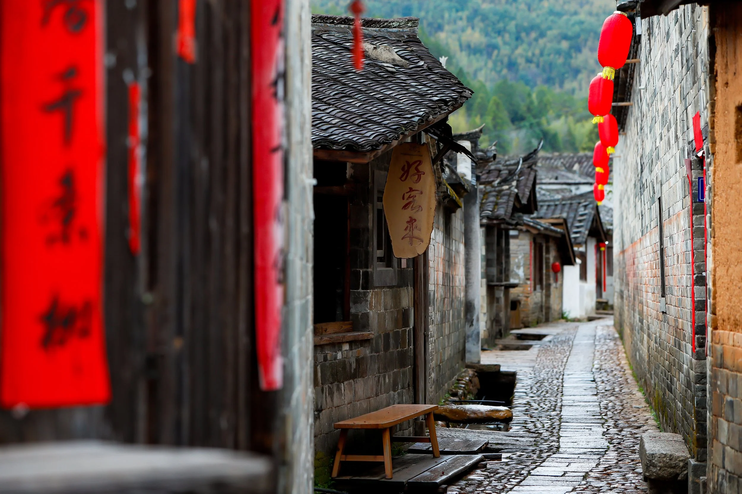 Group of people practicing Tai Chi in a traditional courtyard garden with trees, a pond, scenic mountains in the background, and traditional Chinese architectural elements.
