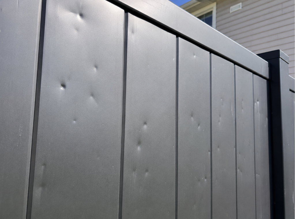 Close-up of a dented aluminum fence panel beside a residential home.