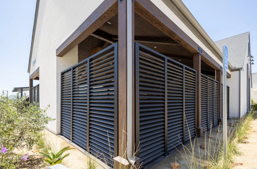 Black steel privacy fence with horizontal slats and natural wood accents along a home exterior.