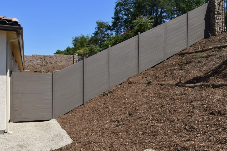 Gray privacy fence installed along a sloped hillside beside a residential property.