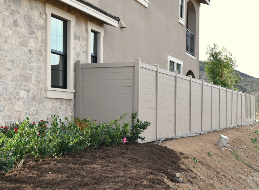 Beige residential privacy fence  installed along a sloped yard beside a home.