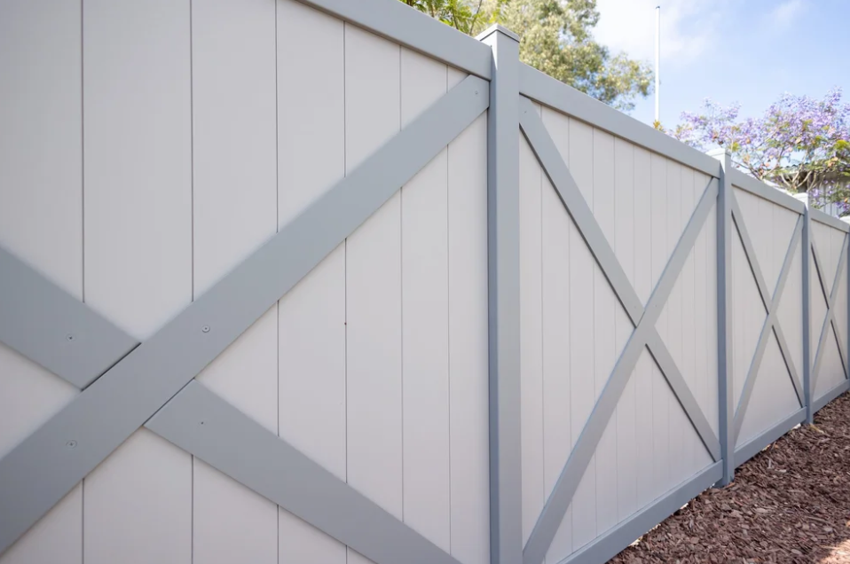White galvanized steel privacy fence with gray cross-brace accents and vertical paneling along a landscaped yard.