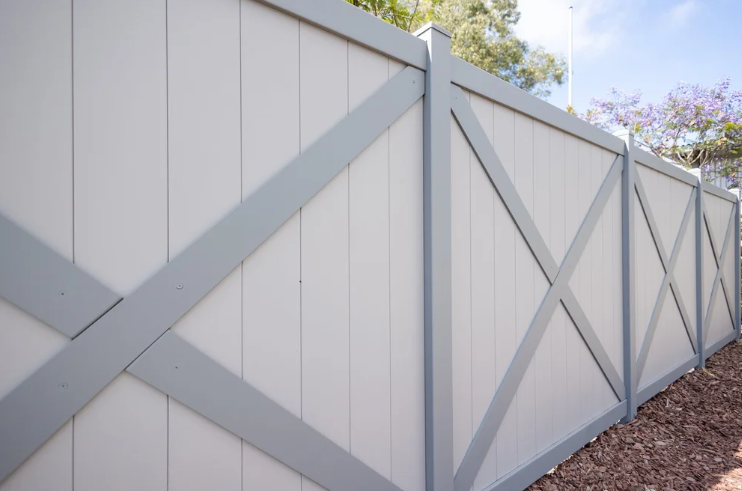 White vinyl privacy fence with decorative crossbeam panels along a yard boundary.