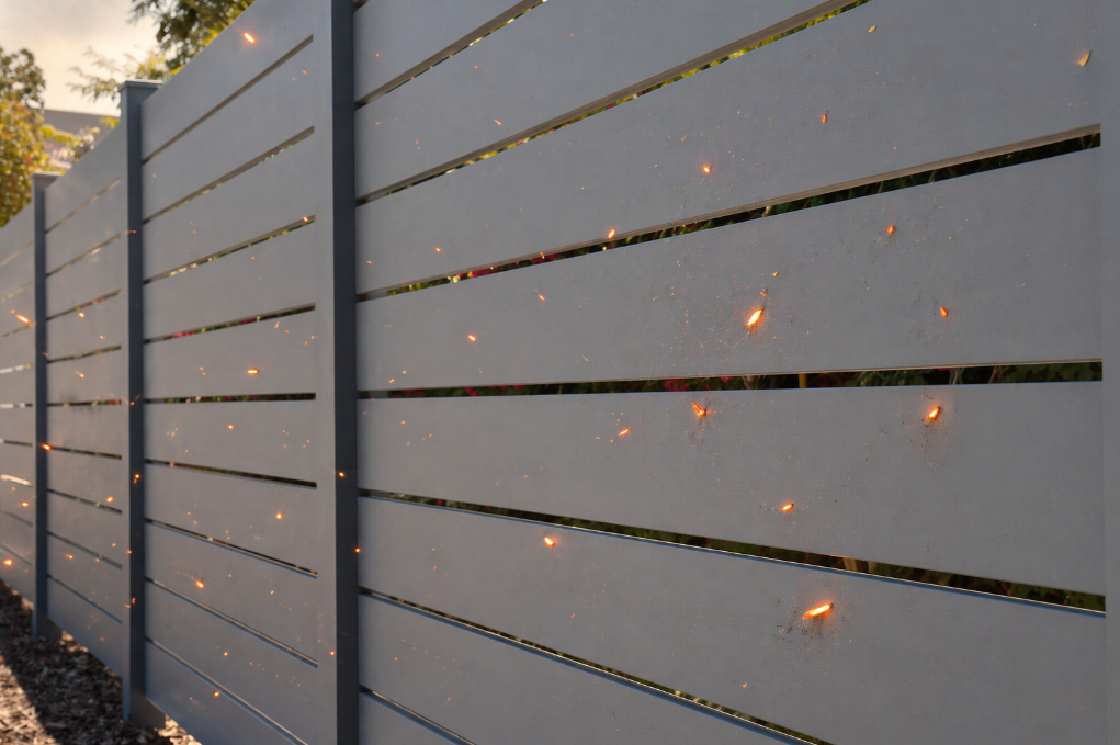 Gray galvanzied steel fence with glowing embers landing on its surface, demonstrating fire resistance.