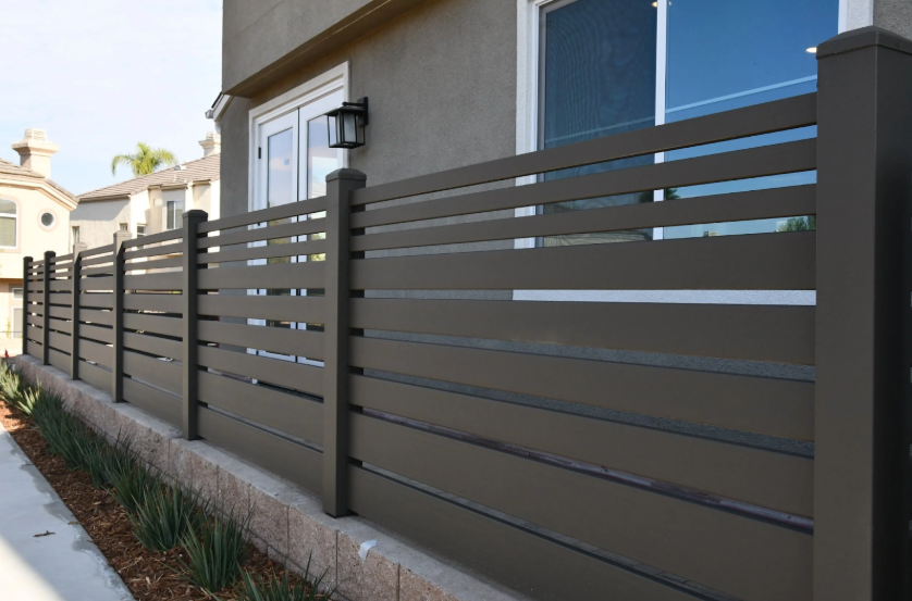 Black steel residential privacy fence with horizontal slats along a home exterior.