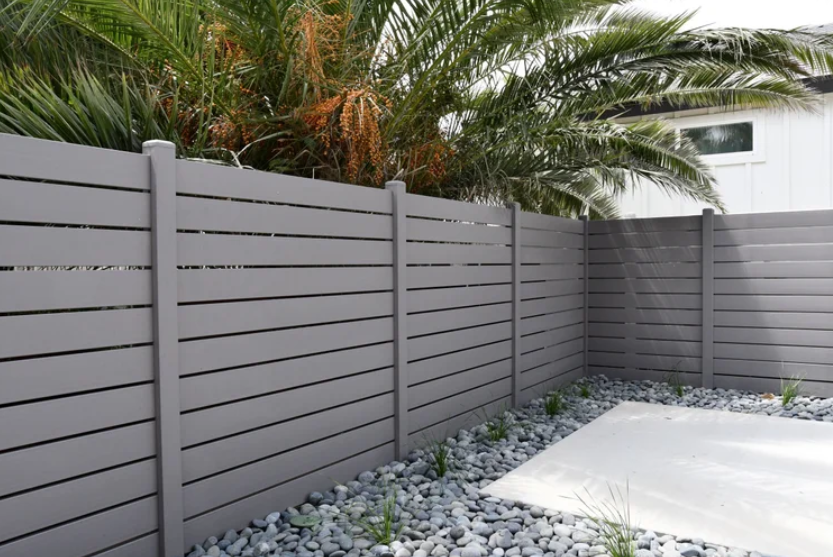 Residential privacy fence with horizontal slats in a landscaped yard.