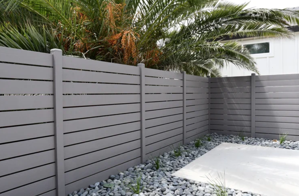 Non-combustible gray galvanized steel fence surrounding a landscaped backyard with rocks and plants.