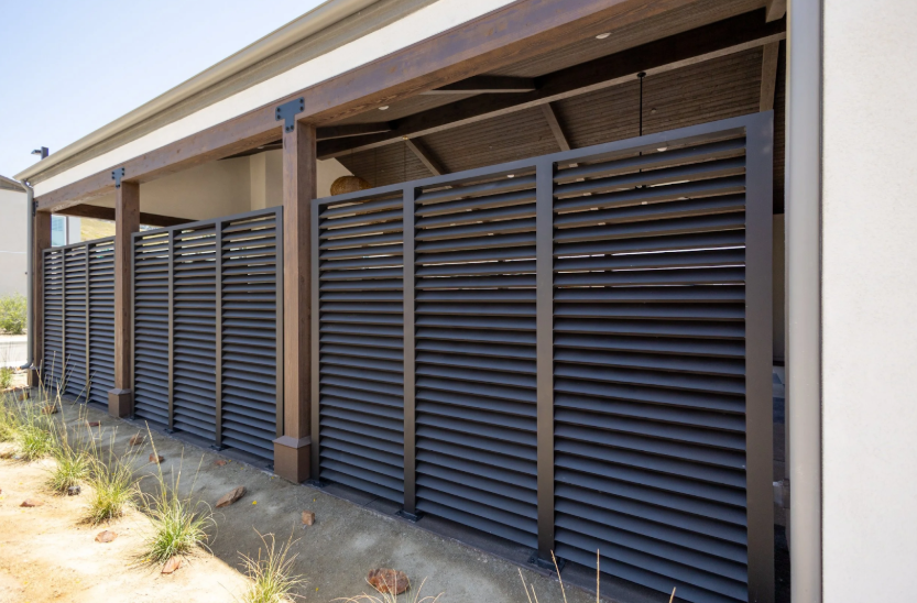 Black steel privacy fence panels with horizontal slats for security along a home exterior.