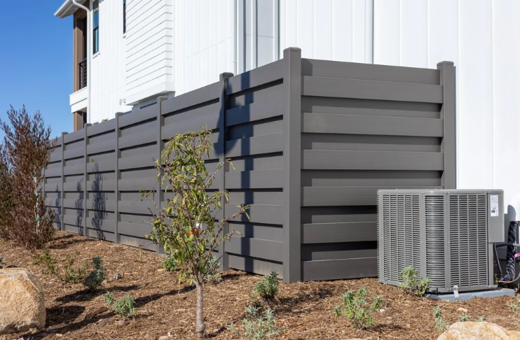 Gray privacy fence installed beside a house with landscaping and an outdoor AC unit.