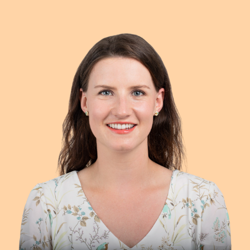 Portrait of a smiling woman with shoulder-length brown hair, wearing a floral top and pearl earrings, against a peach background.