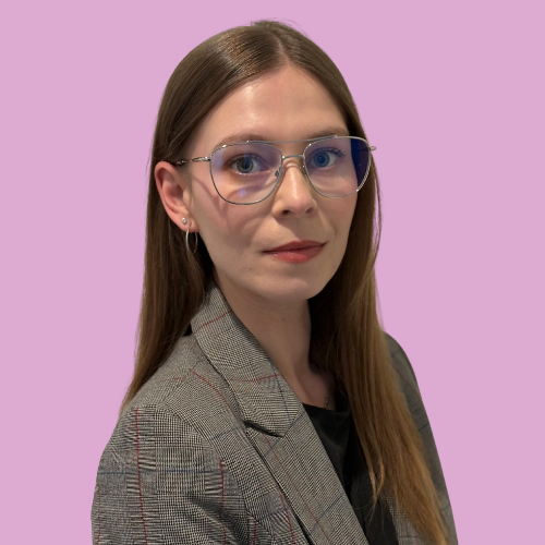 A woman with brown hair, wearing a dark blue shirt, smiling against a light purple background.
