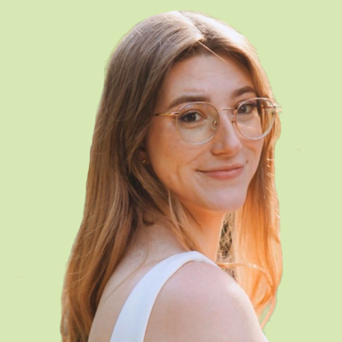 A young woman with light brown hair, glasses, and a nose piercing, smiling against a light green background.