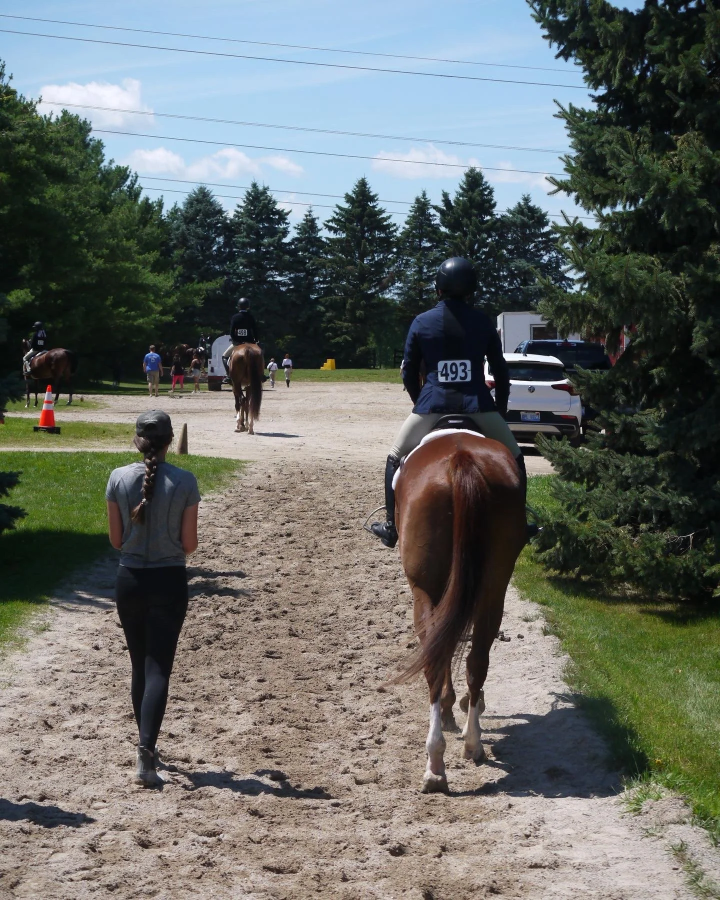 People riding horses in an outdoor riding area, with trees and a clear sky in the background.