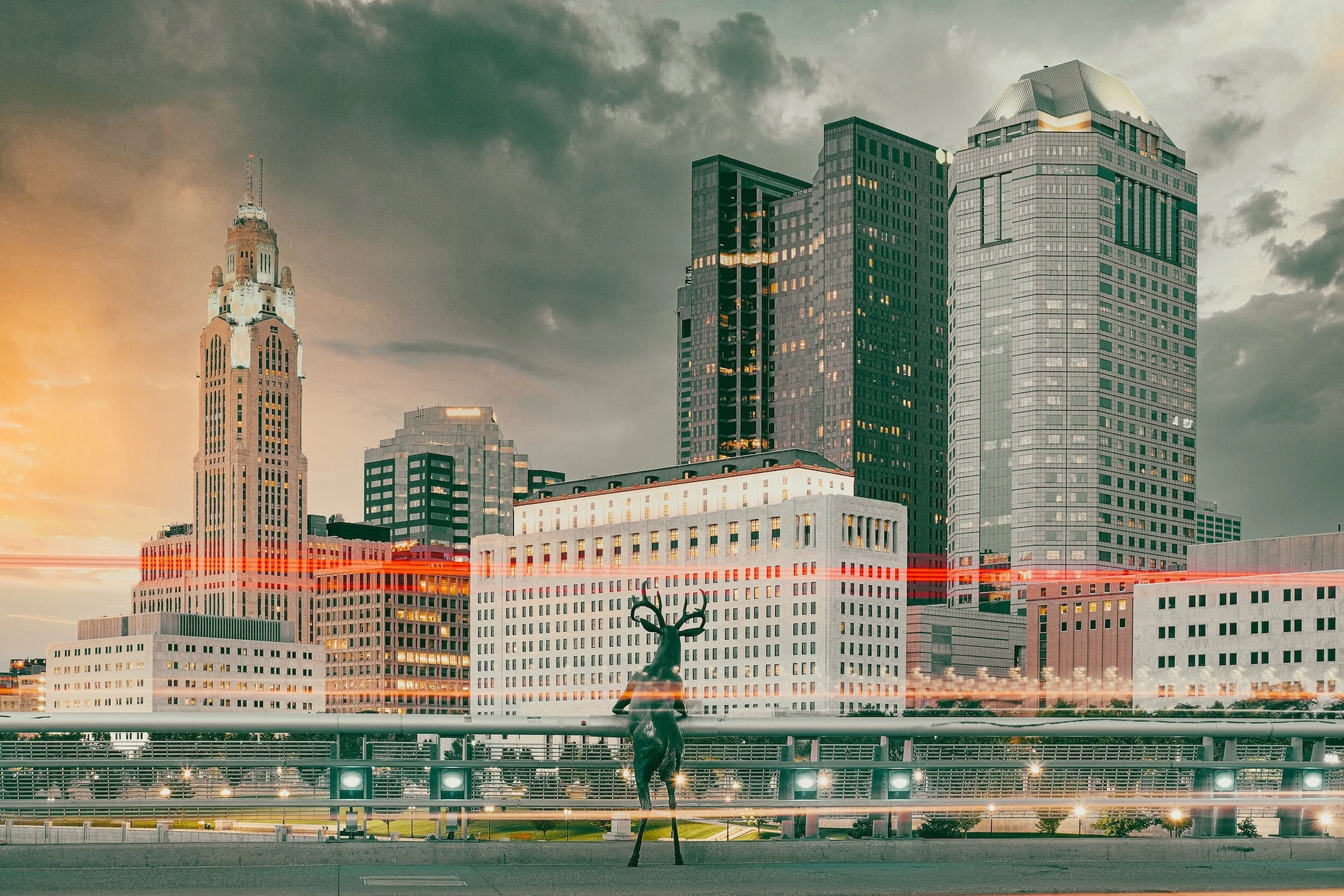Skyline of downtown Cleveland, Ohio, with prominent Terminal Tower and modern high-rise buildings, during dusk with streaks of red and white light from moving vehicles.