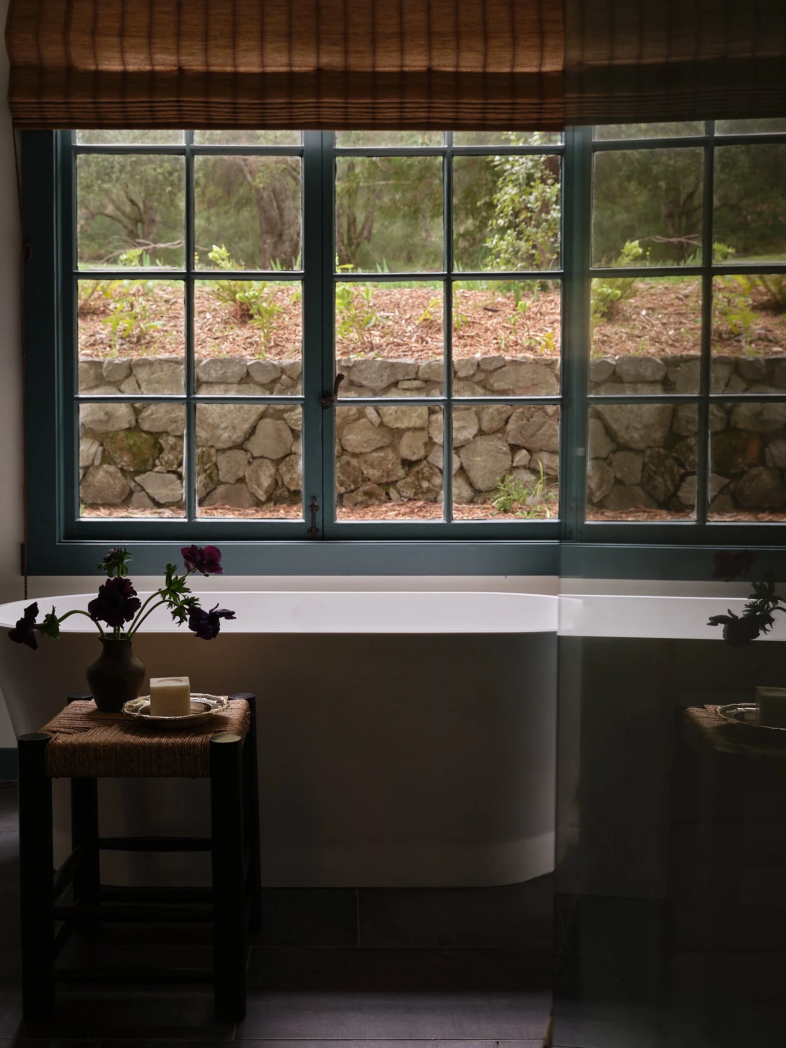 Interior view of a room with a large window showing an outdoor garden with rocks, soil, and green plants.