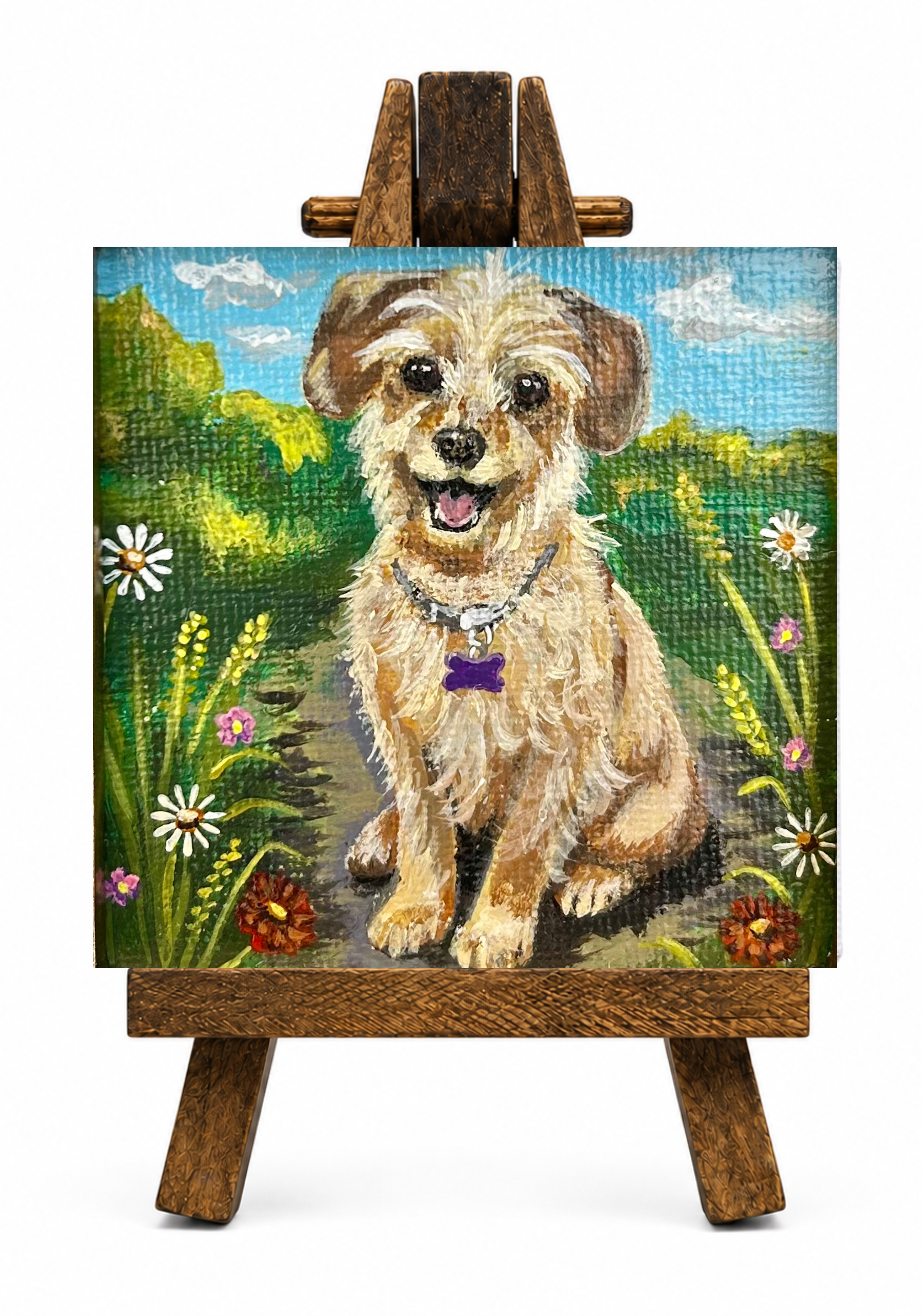 Painting of a happy puppy sitting in a field of flowers with a blue sky and clouds in the background, displayed on a wooden easel.