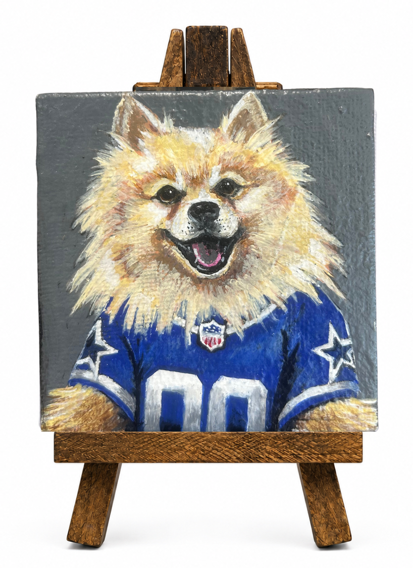 A painting of a dog with a fluffy golden coat, wearing a Dallas Cowboys football jersey, displayed on a wooden easel.
