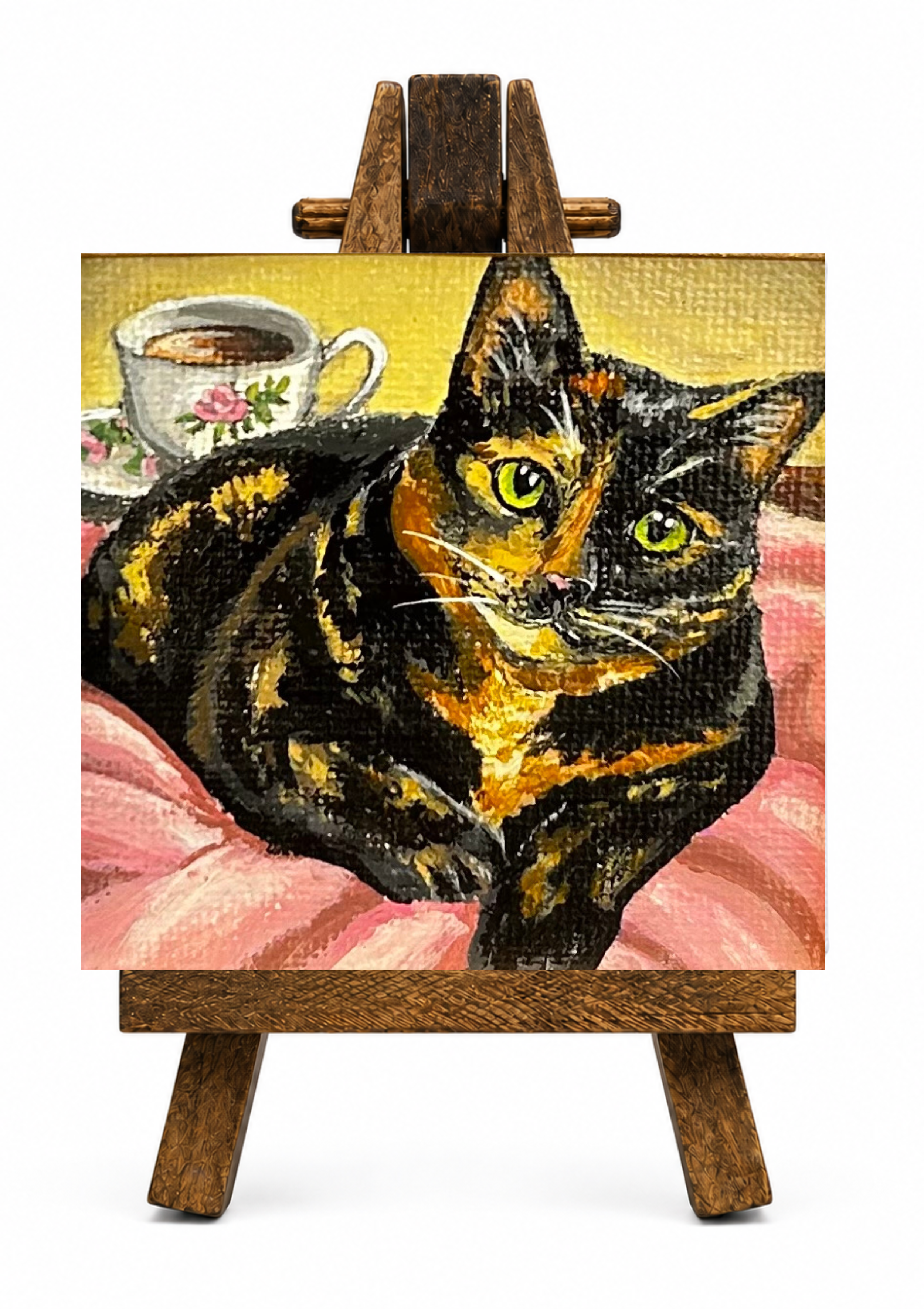 Painting of two black and orange cats on an easel, with a yellow background and a cup of coffee and pink flowers in the background.