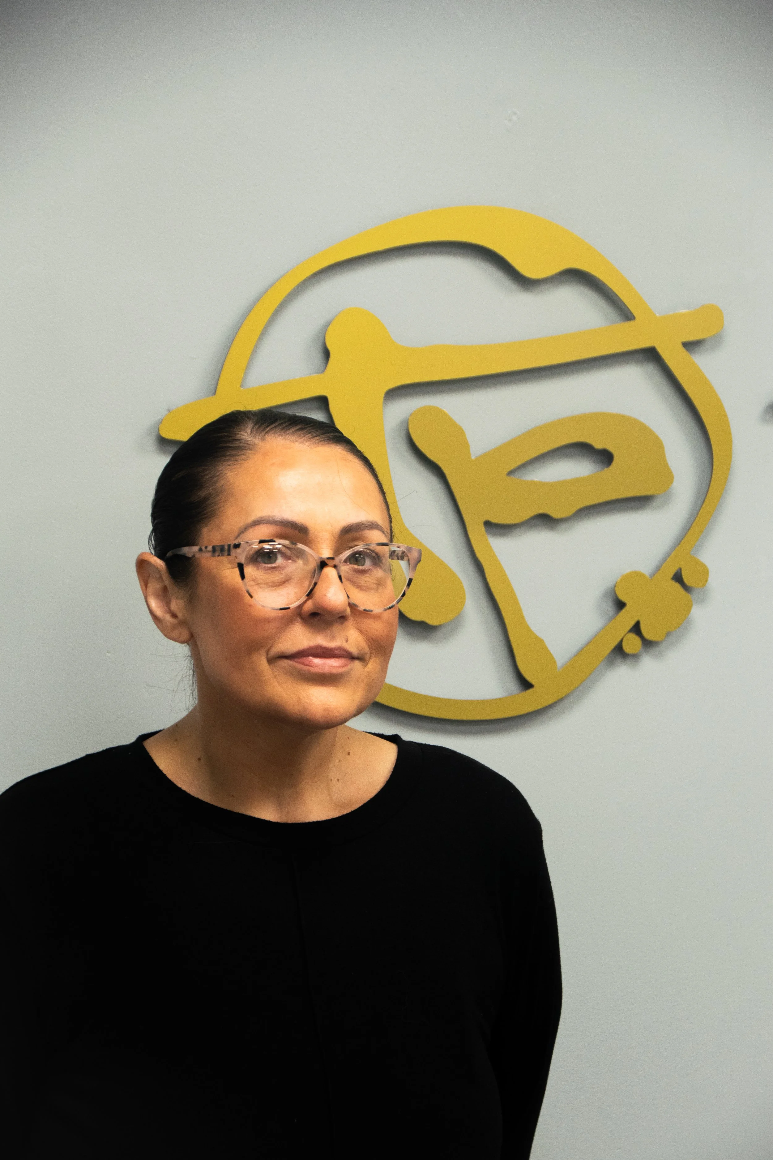 A smiling woman in a chef uniform standing in front of a wall with a sign that says "Terry's Patisserie".