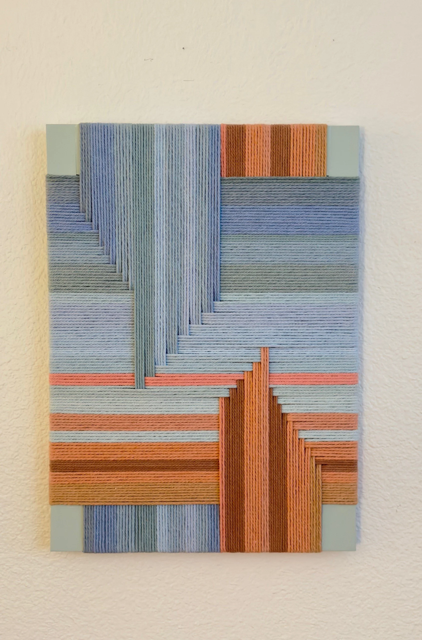Colorful abstract artwork made from woven or layered strips in shades of blue, orange, and brown.