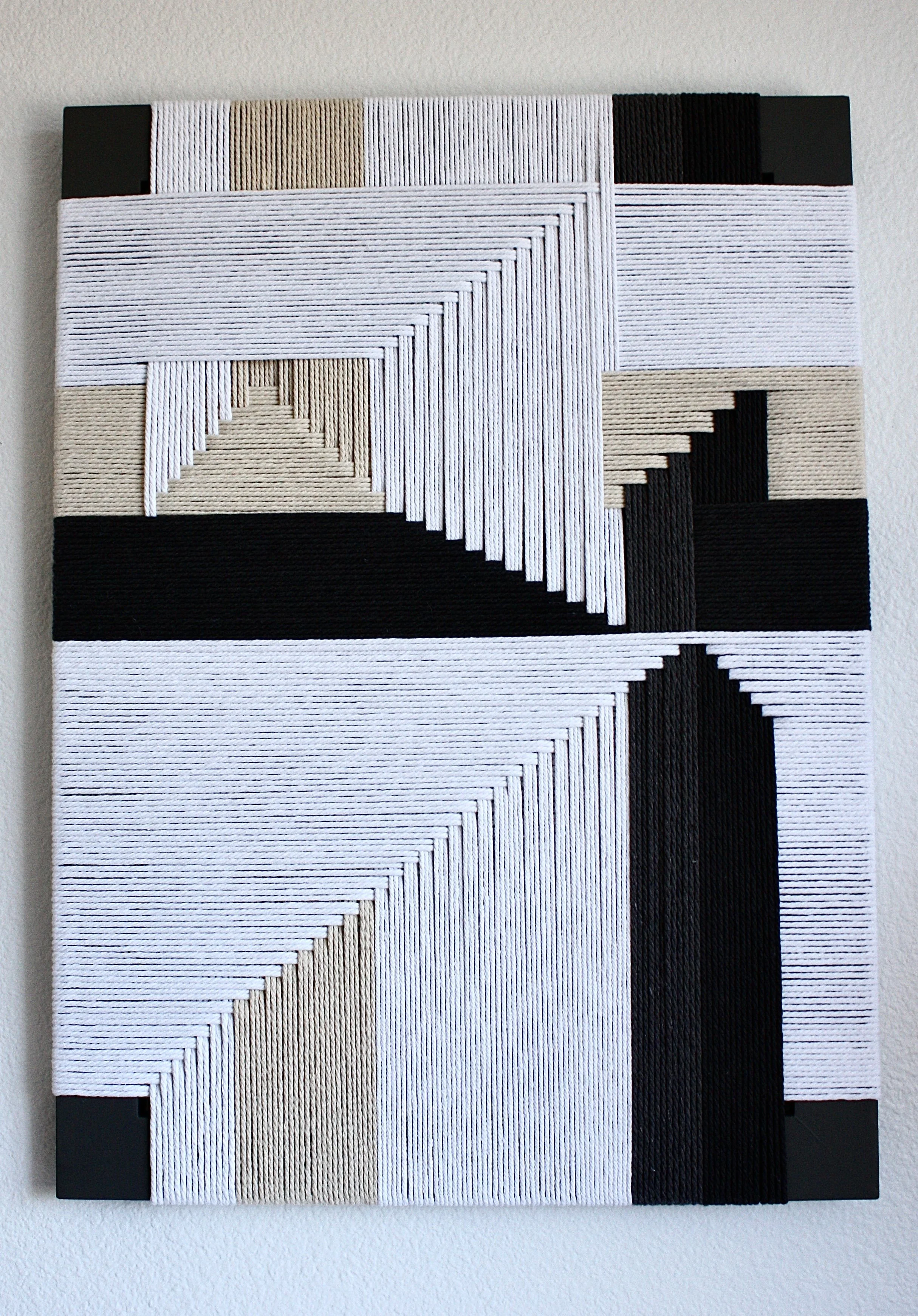 Geometric wall art with black, white, and beige threads arranged in symmetrical pattern.