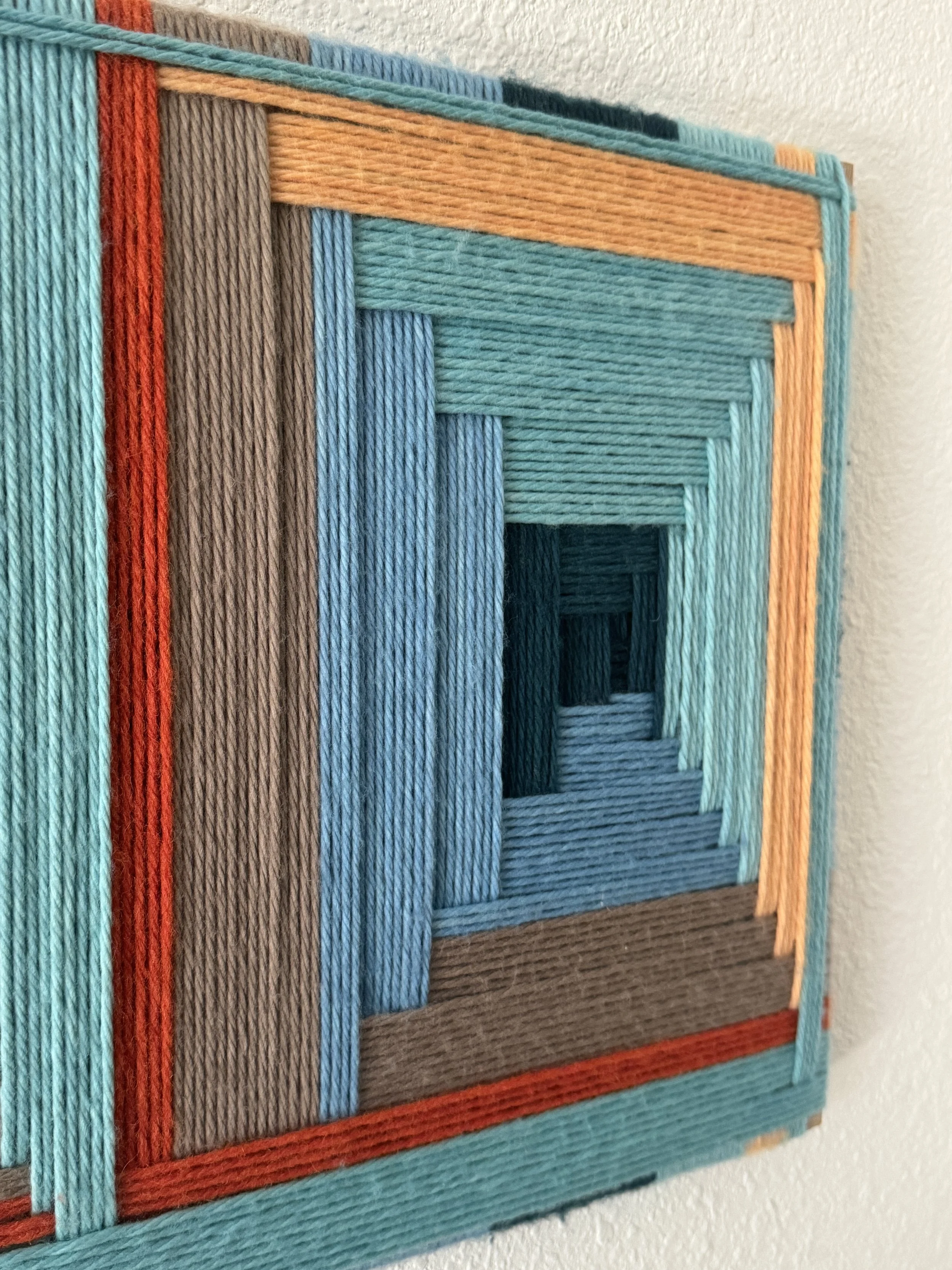 Colorful wall art made of layered yarn arranged in a geometric, square pattern creating a tunnel effect.