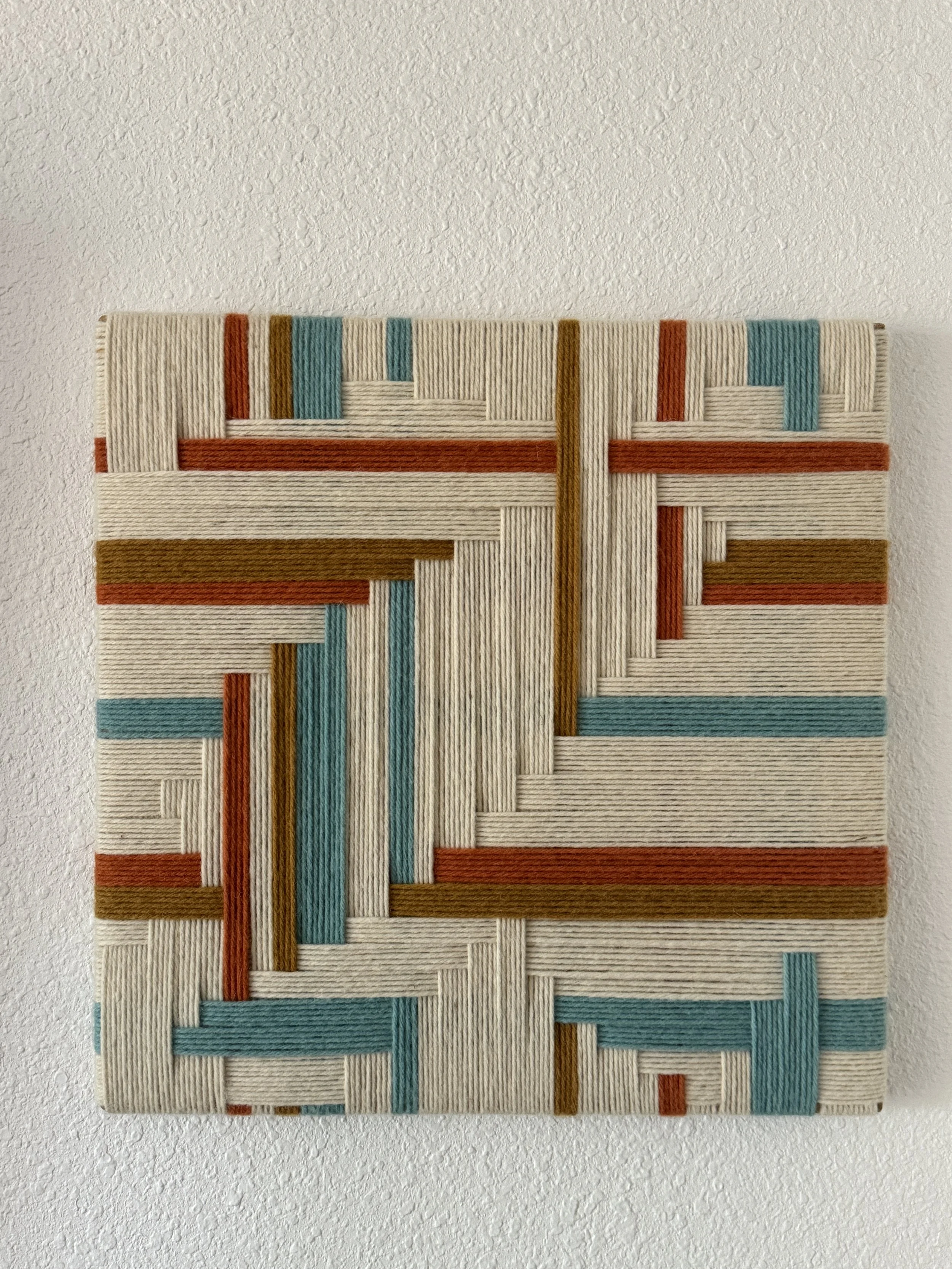 Colorful woven textile wall art with geometric pattern on a white wall.