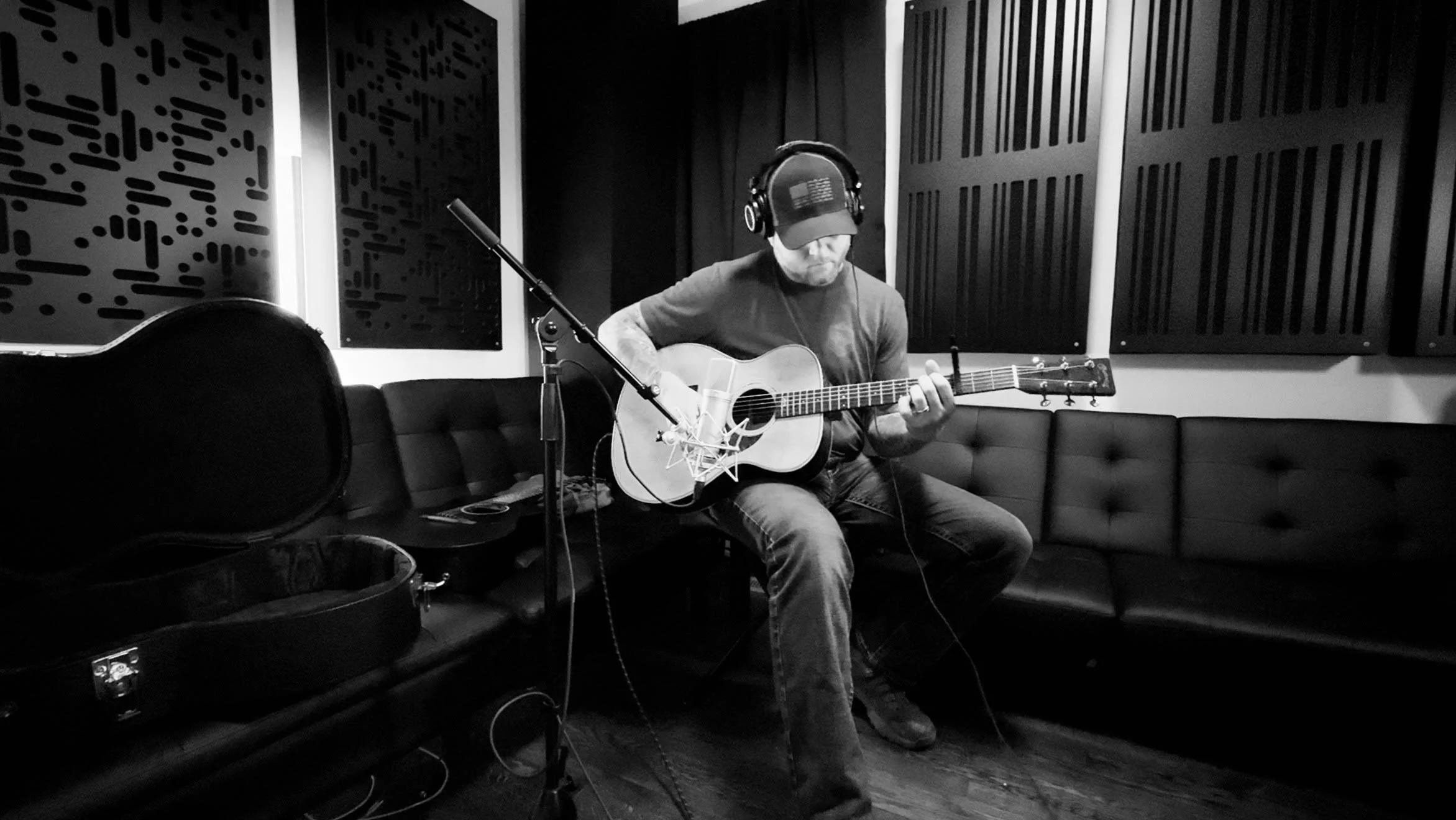 Music recording session at Samples Studios with professional singer and guitarist Josh Fosdick. Josh is wearing headphones and playing an acoustic guitar. Samples Studio has custom acoustic panels on the walls and a Neumann microphone in charlotte nc