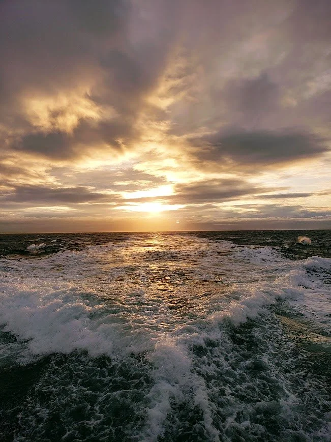 Sunset over the ocean with clouds and waves in the water.