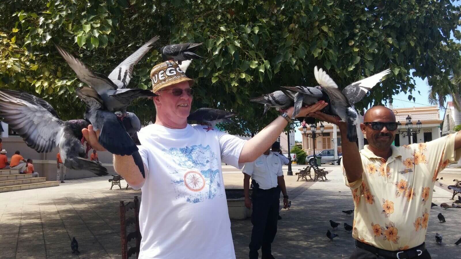 A man feeding pigeons at central park on of many stops on the Explore the Best of Puerto Plata shore excursion by Puerto Plata Adventures.