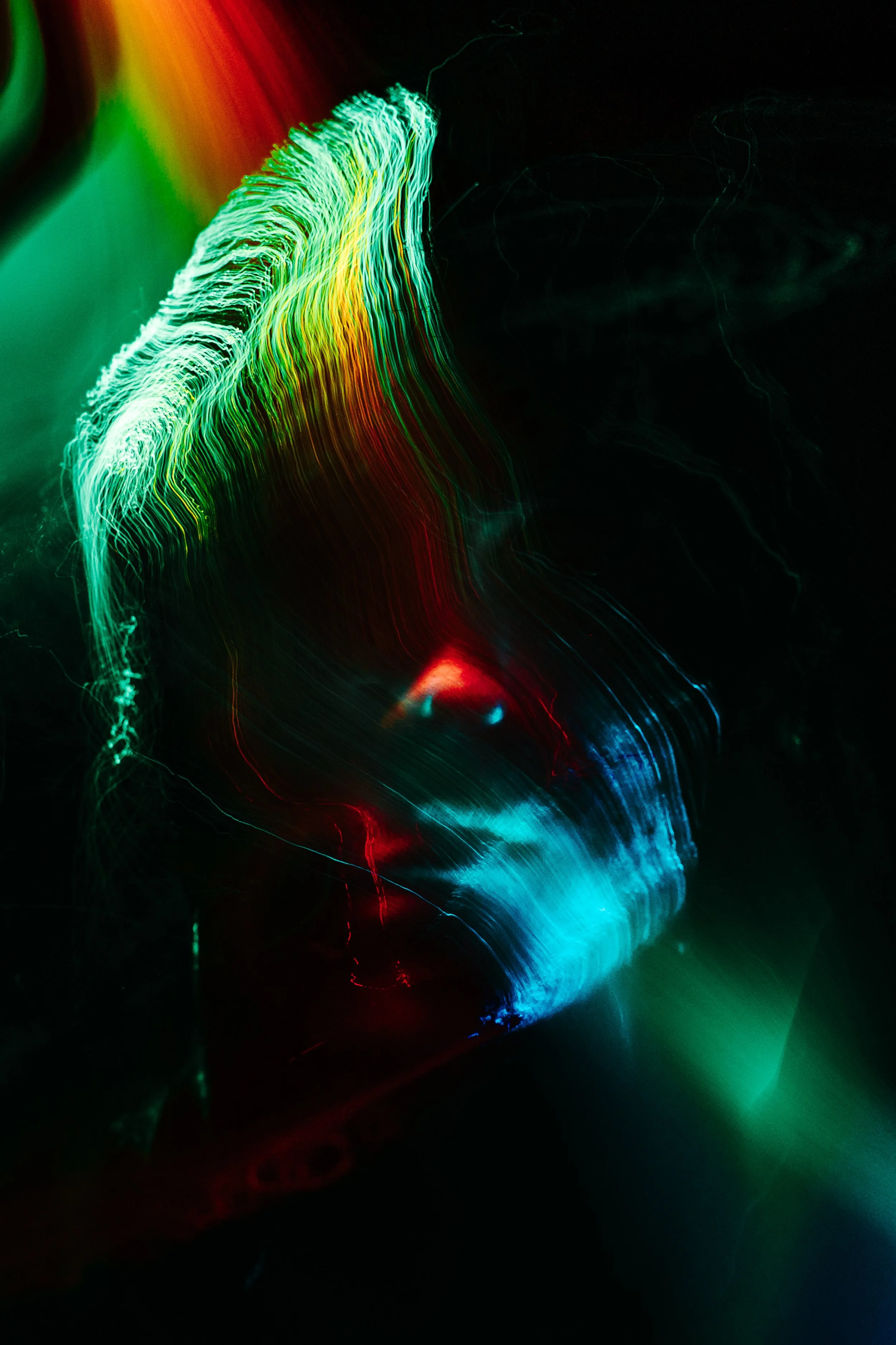 Abstract light trails in green, red, blue, and orange colors against a dark background, creating a dynamic, flowing pattern.
