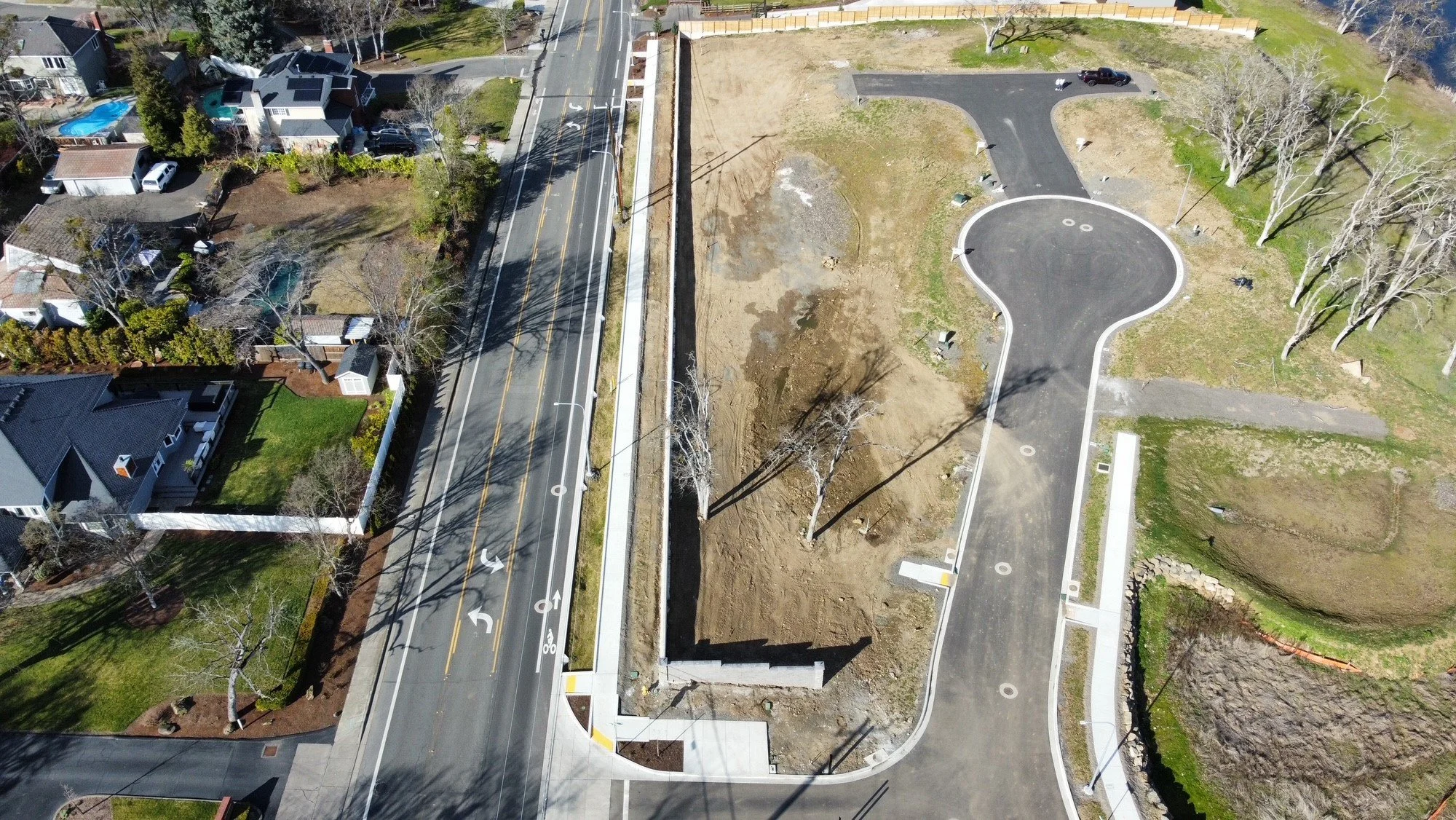 Aerial view of the neighboring subdivision and our new neighborhood under construction, surrounded by houses, trees, and a body of water in the background.