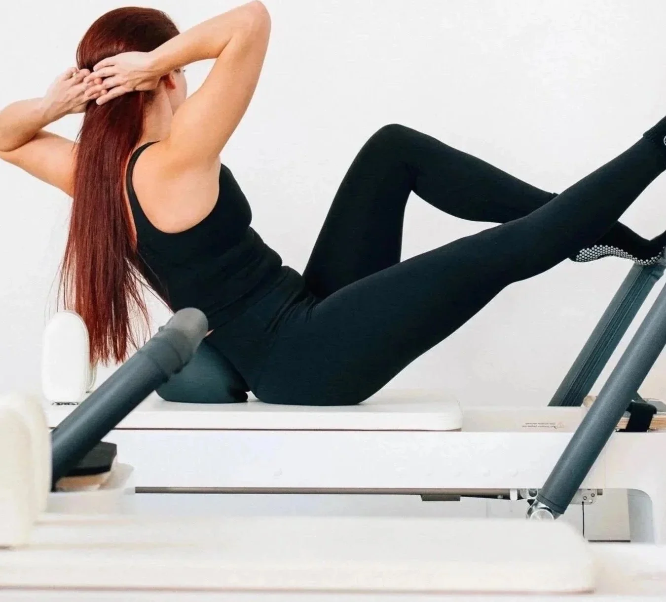 Woman exercising on a reformer Pilates machine in a studio with white walls