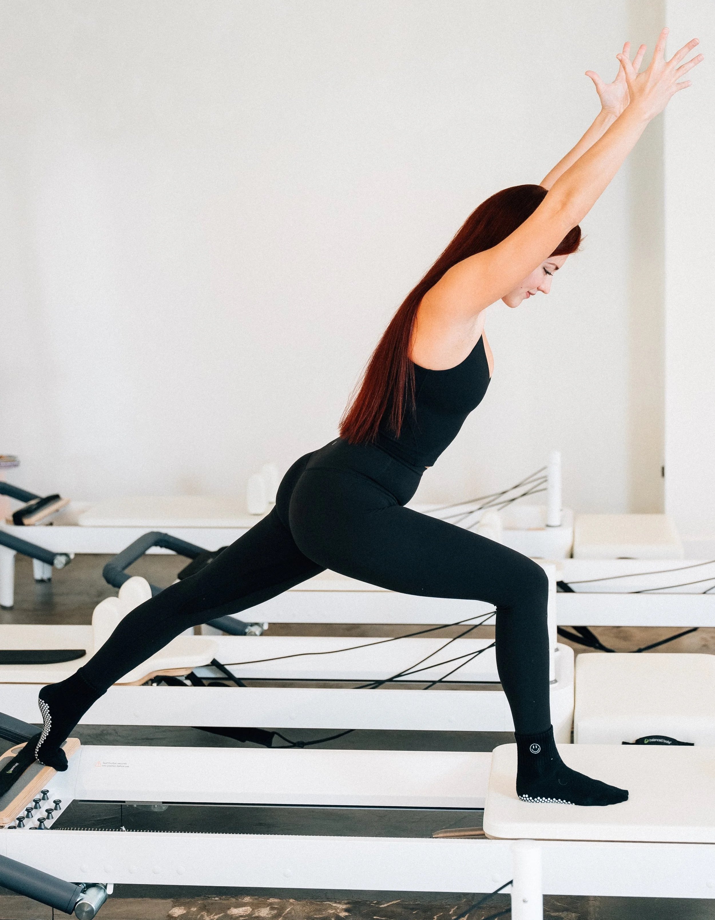 A woman performing a lunge exercise on a reformer machine in a fitness studio.