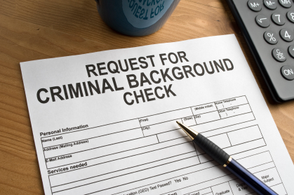 A form titled 'Request for Criminal Background Check' on a wooden desk, with a pen, a calculator, and a blue mug nearby.