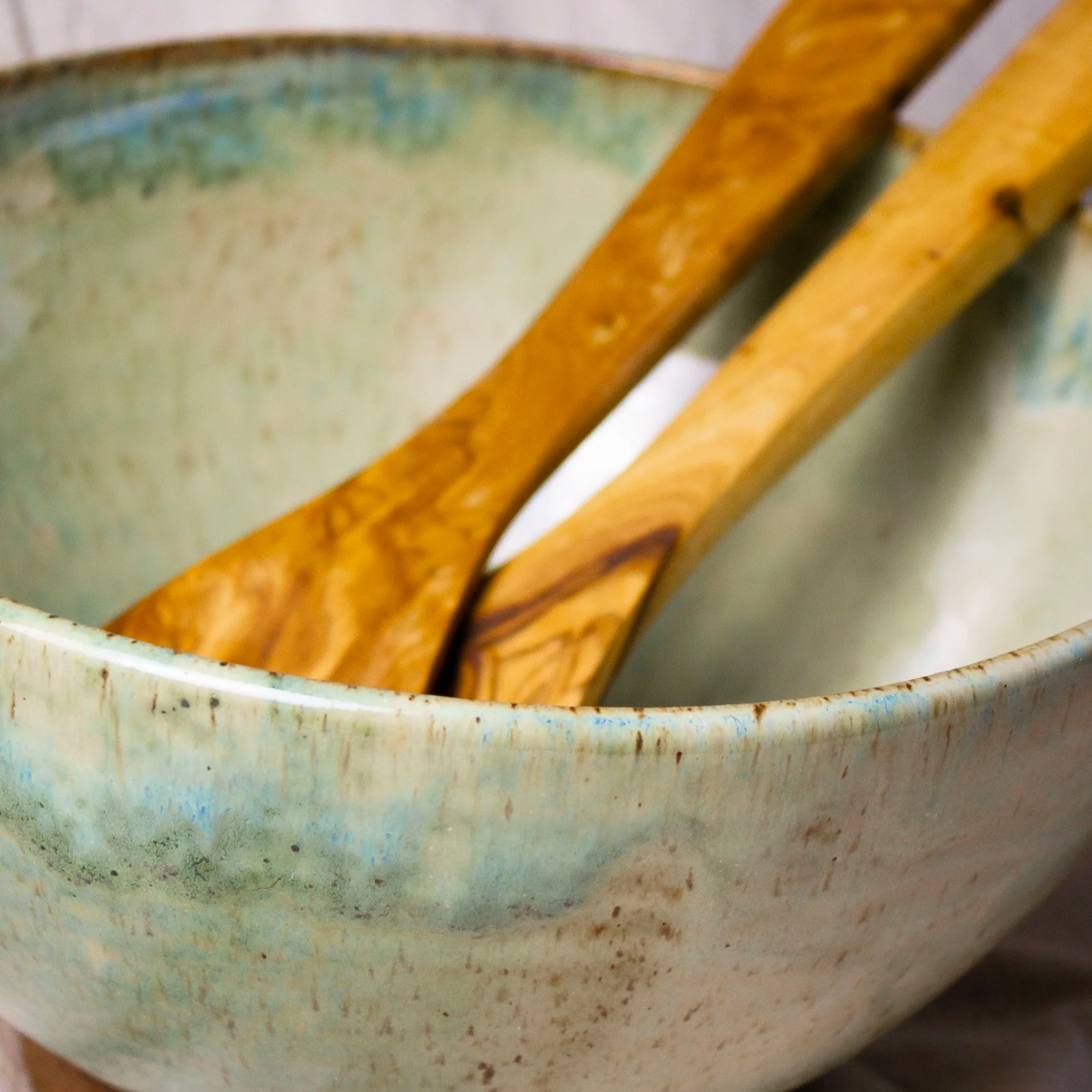 Close-up of wooden kitchen utensils soaking in a weathered turquoise ceramic bowl