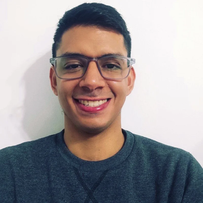 Young man with glasses smiling in portrait against white background.