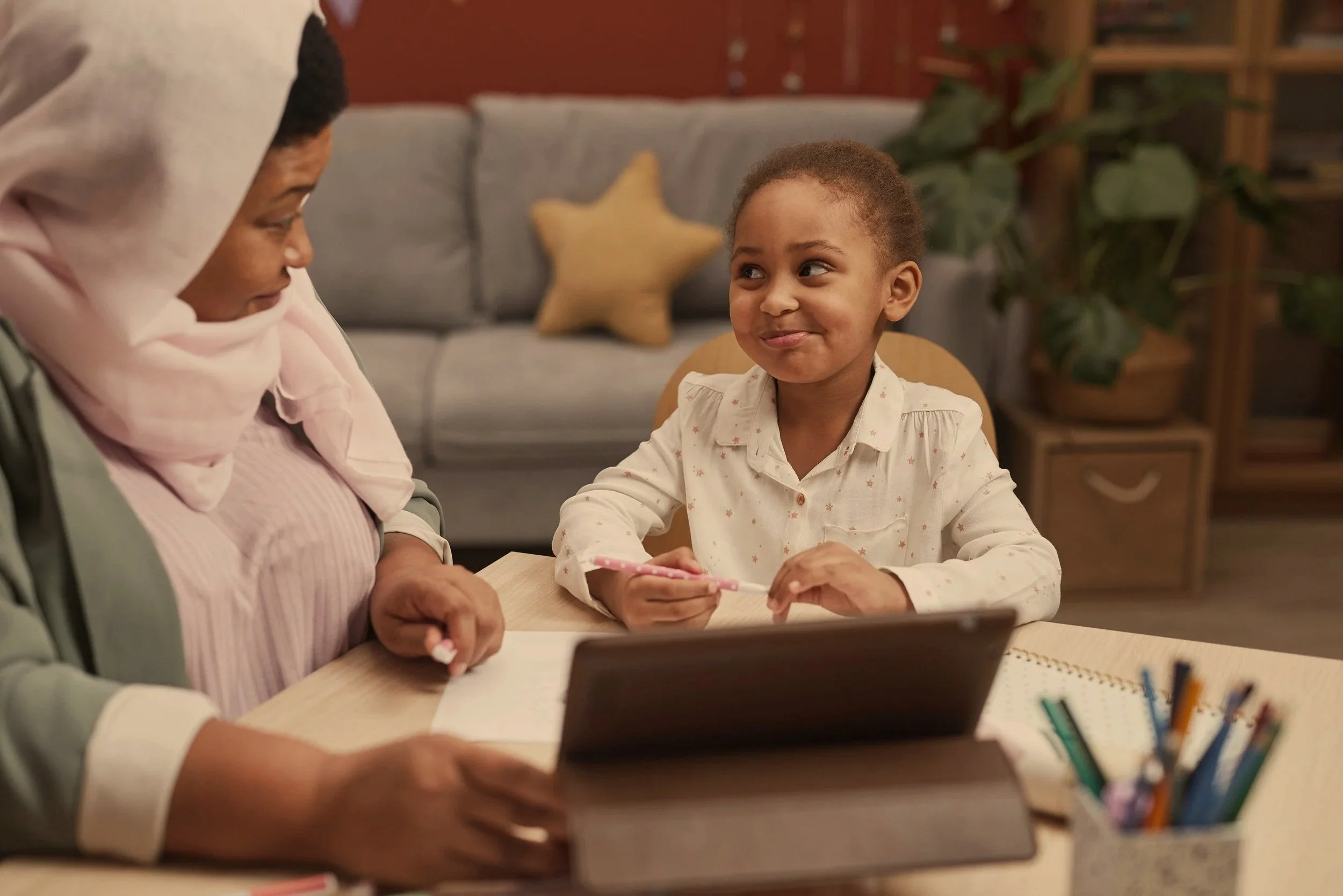 Plan moyen d'une table avec une enfant et une interprète. On comprend que l'orthophoniste est en face. L'interprète est active, tout le monde sourit et interagit.