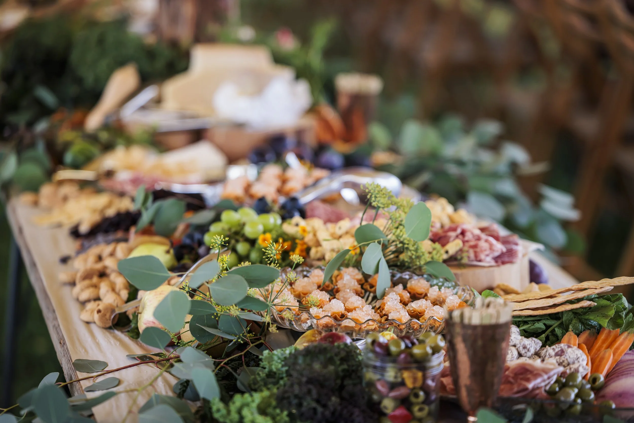 A grazing table spread with cheese, cured meats, fruit and greenery