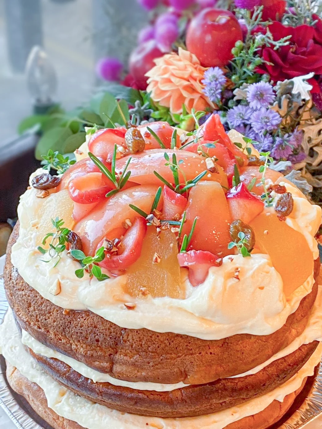An anniversary cake topped with seasonal fruit and rosemary, and a bouquet